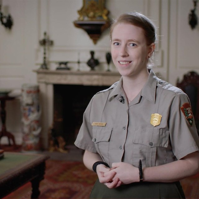 Ranger talks to camera in front of fireplace and gold folding screen