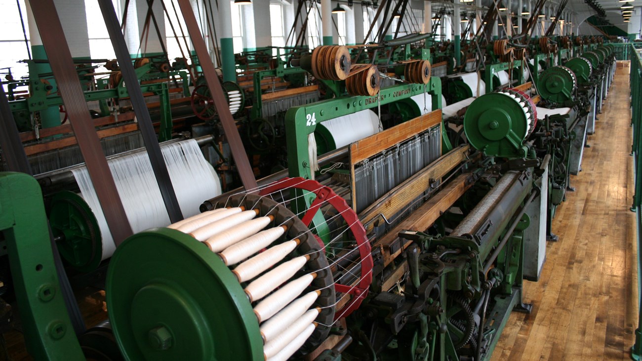 A weaver stands by a row of power looms