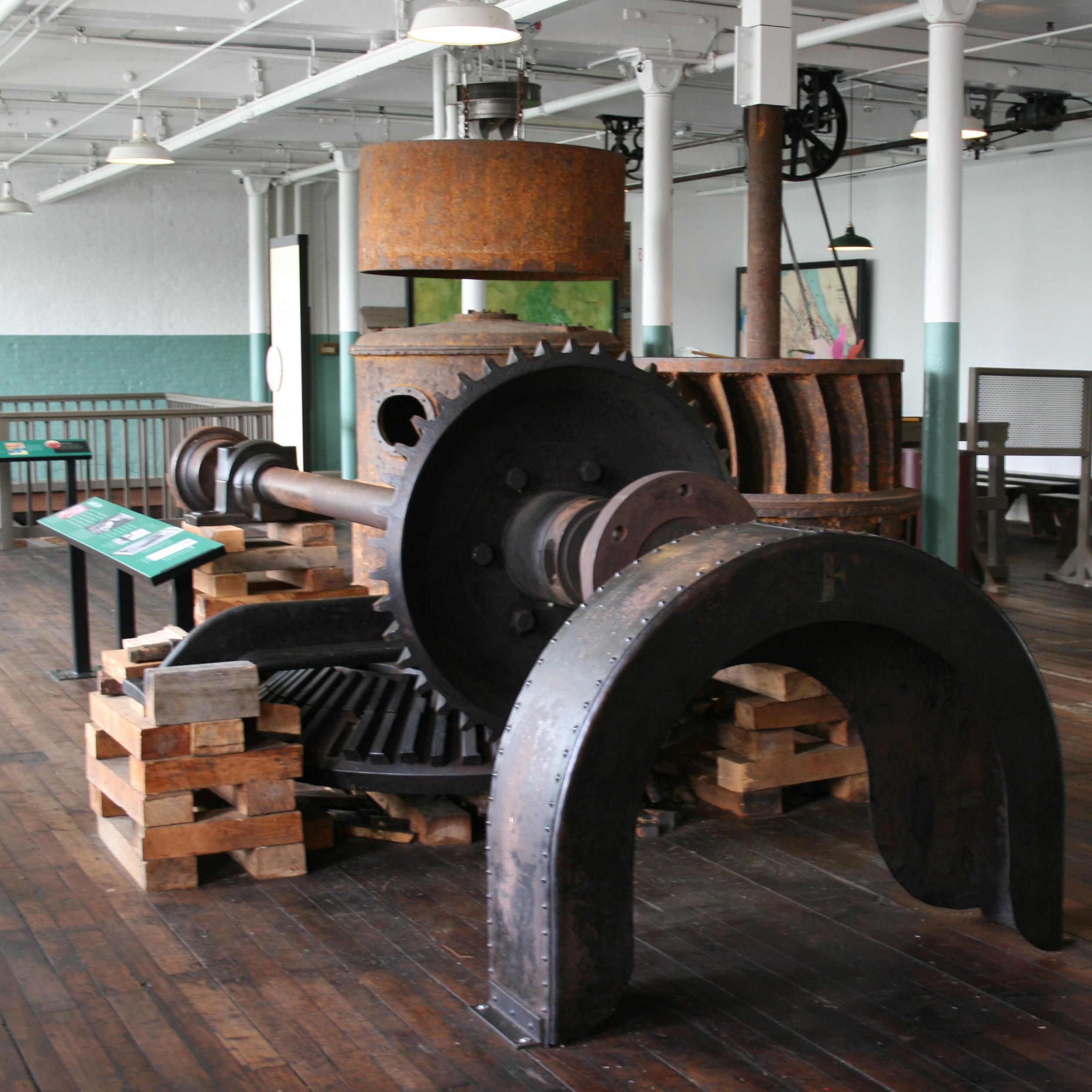 The interior of a historic mill with gears, turbines, and machines on display in the center