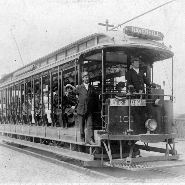 A full trolley riding along tracks toward the camera, black and white photo