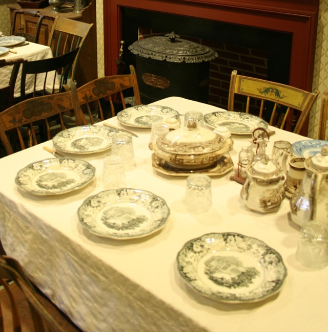 A dining room full of plates, tables, chairs and silverware