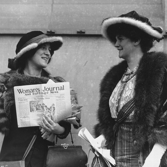 Two suffragists conversing while handing out the Woman's Journal newspaper on the street.