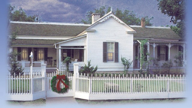 A Christmas wreath hangs on the gate of the Boyhood Home while lamplight shines from the windows.