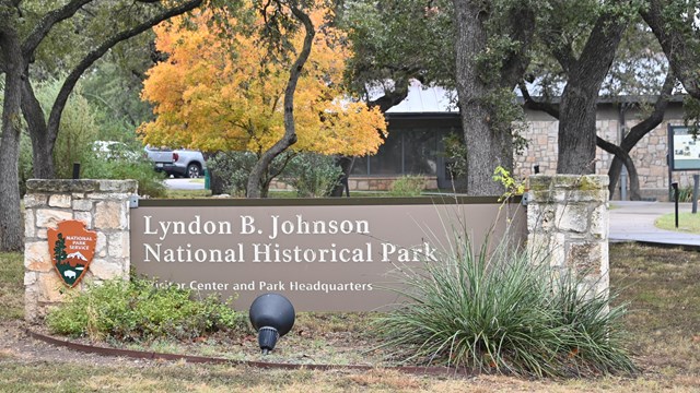 A large brown sign in front of a stone building reads "Lyndon B. Johnson National Historical Park"