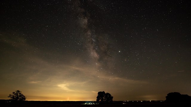 View of stars in a dark sky above wide-open ranchland.