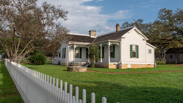A photo of a small, white house with white picket fence.