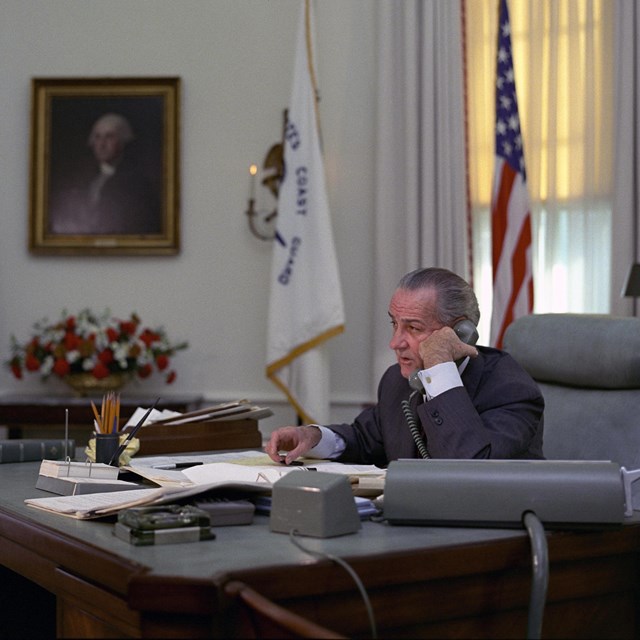 Lyndon Johnson talking on his desk phone in the Oval Office.