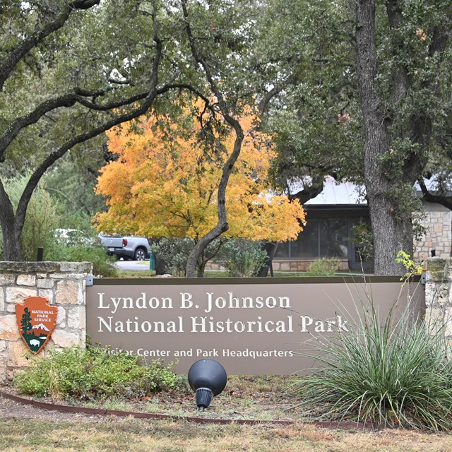 A large brown sign in front of a stone building reads 