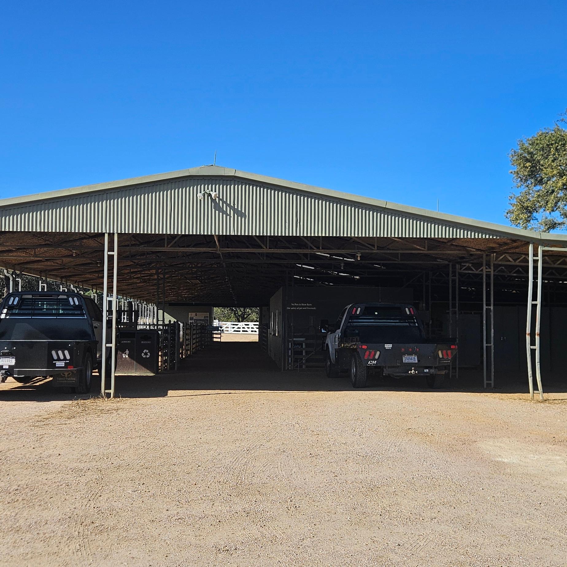 Green barn with ranch vehicles parked in front. Walk way in middle of barn.