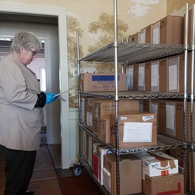 A staff member holds a clipboard while viewing multiple shelves of boxes.