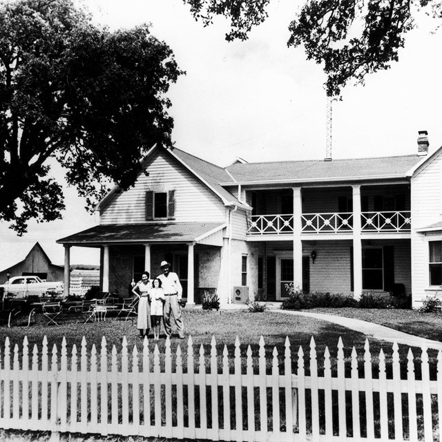 Lady Bird, ten-year-old Lynda, and Lyndon Johnson standing in front of a two-story frame house.
