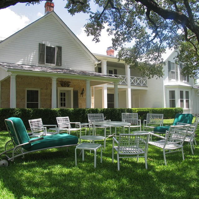 White chairs form a circle on a green lawn in front of a large, white house.