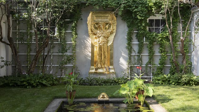 A gilded statue of an angel stands behind a narrow reflecting pool