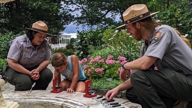 Two park rangers kneel next to child looking in a microscope