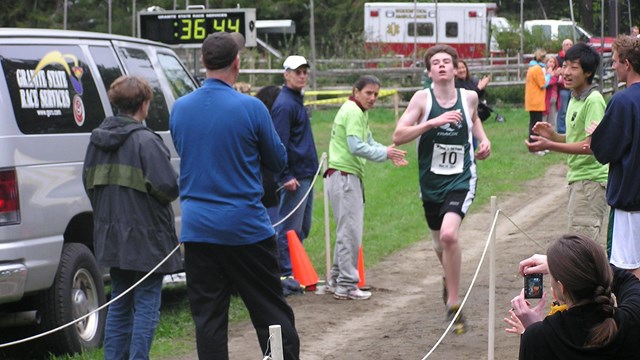 runner crosses finish line on park carriage road with race timer behind