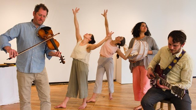 three dancers and two musicians perform on a hardwood floor