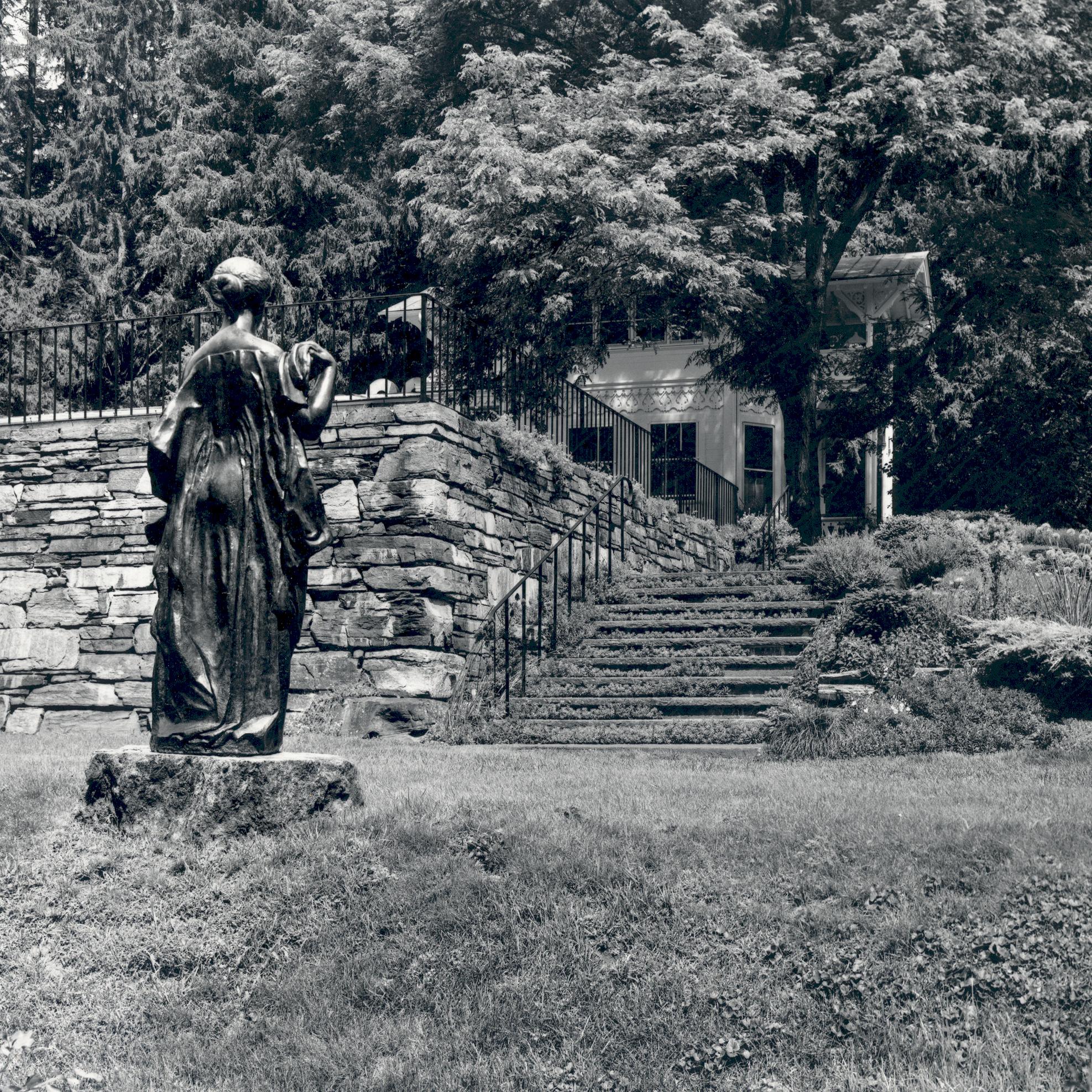 black and white photo of steps leading up to Rockefeller pool with bronze statue of a woman on left