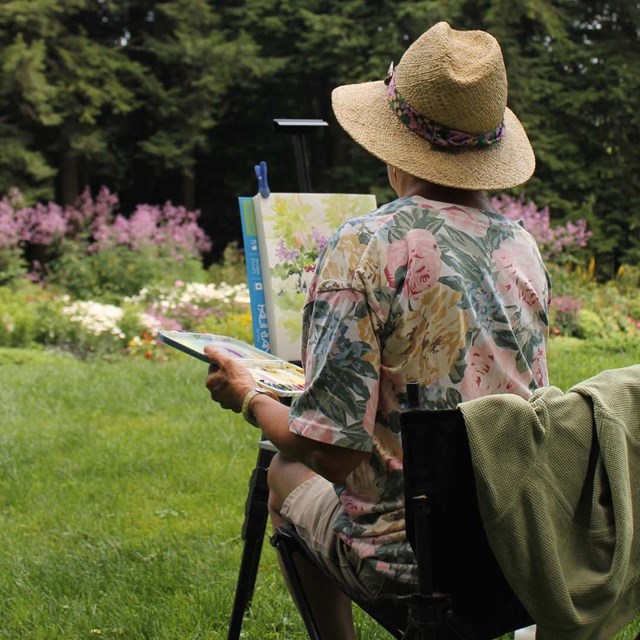 artist paints in garden with back turned to camera