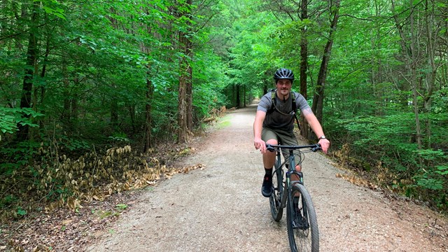 A young man riding a bike on a gravel trail. 