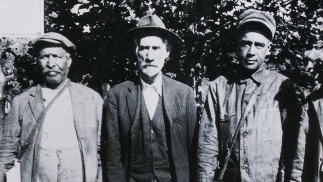 Black and white photo of 5 men standing in a row holding lanterns and long sticks.