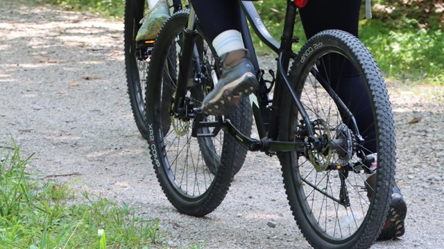 Two people ride bikes on a gravel path.