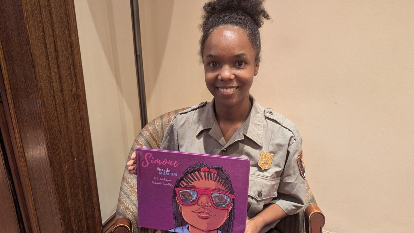 NPS Ranger sits in a chair holding a magenta colored book