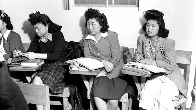 Black and white photo of three young women working at desks at Manzanar