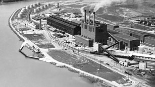 Black and white photo of industrial complex by a river.
