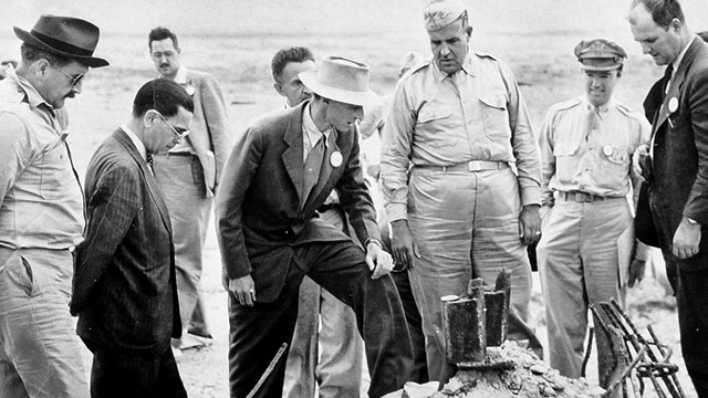 A black and white photo of a group of men looking at something on the ground. 