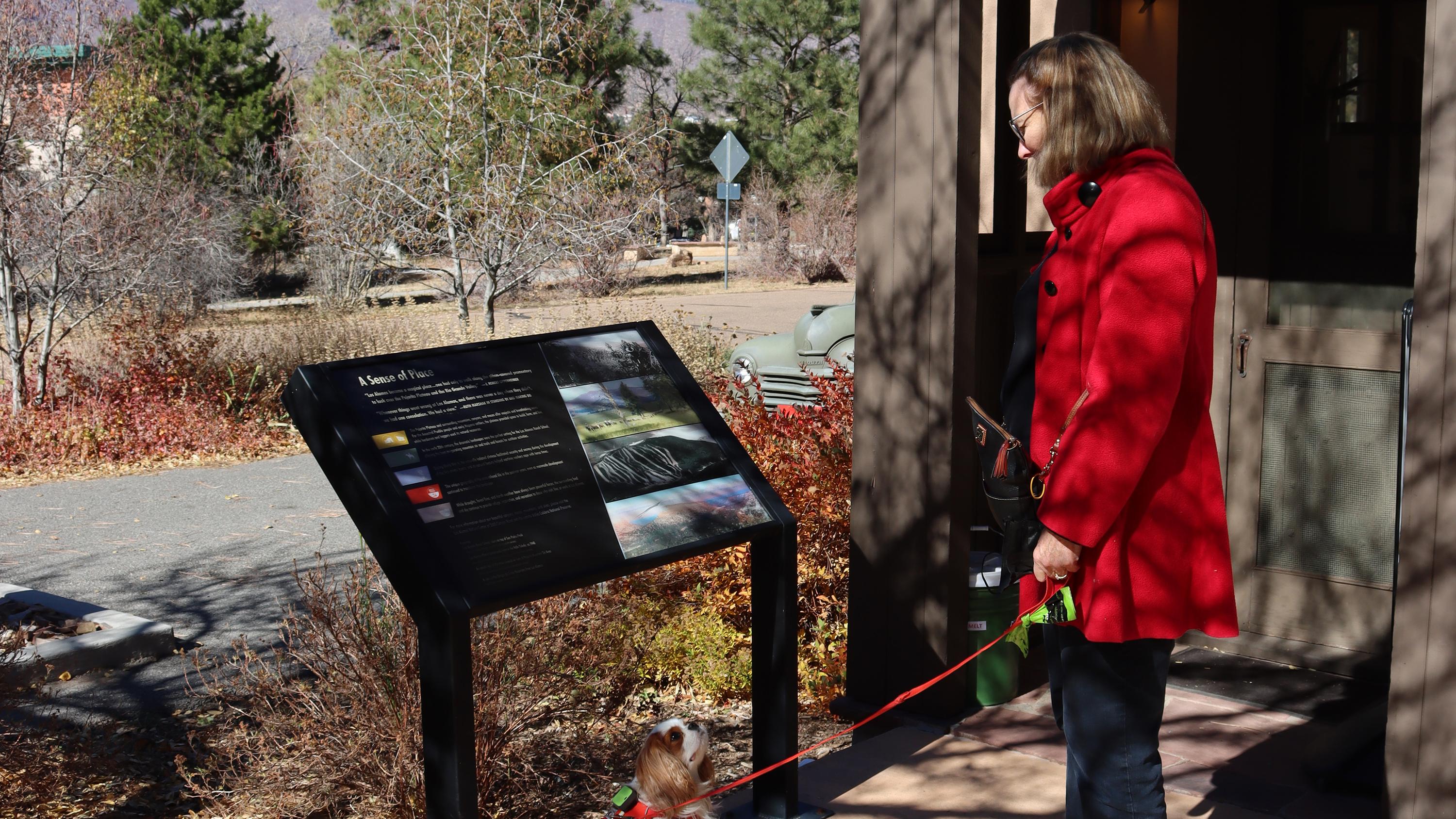 A lady in a red coat reads a wayside.