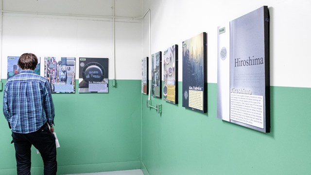 A man in a blue plaid shirt reads exhibit panels in a green and white room.