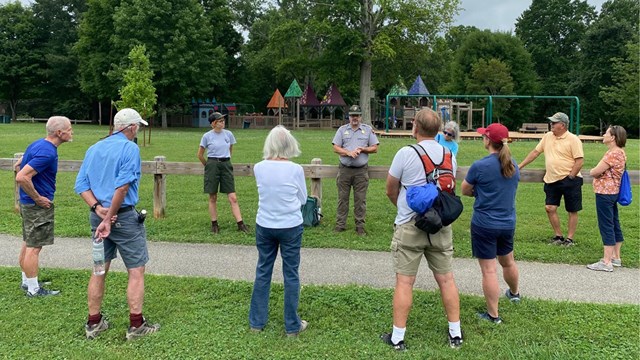 Several people standing around two rangers in a city park.