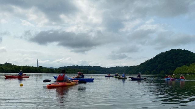 Several kayakers on a river. Puffy clouds fill the sky. 