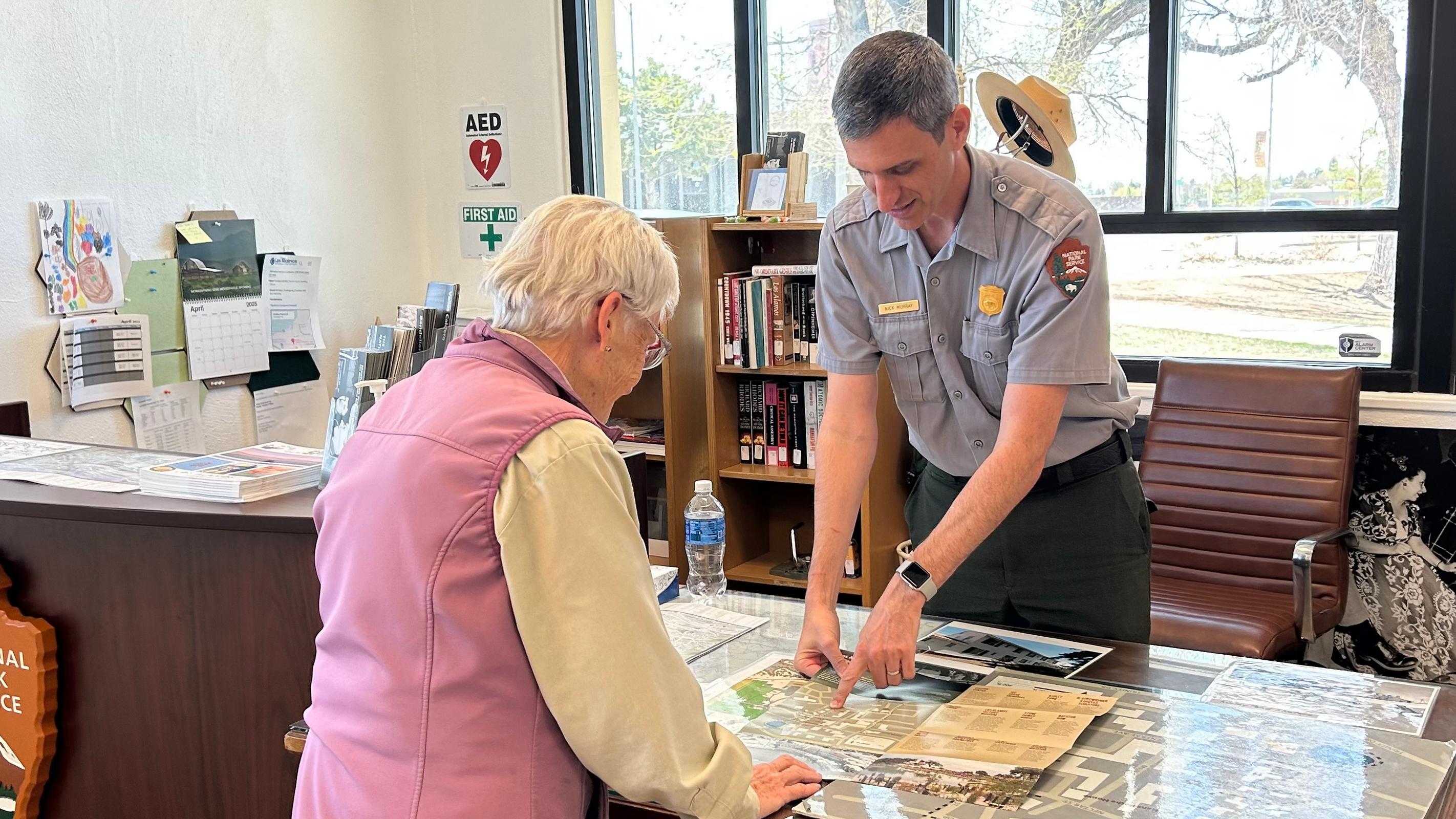 A park ranger points out something on a map to a visitor.