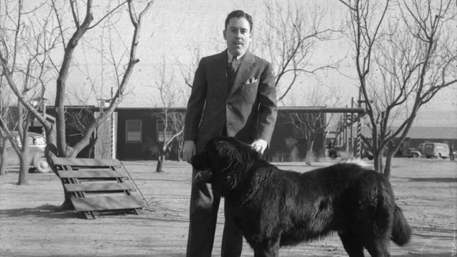 A black and white photo of a man with a large black dog on a leash.