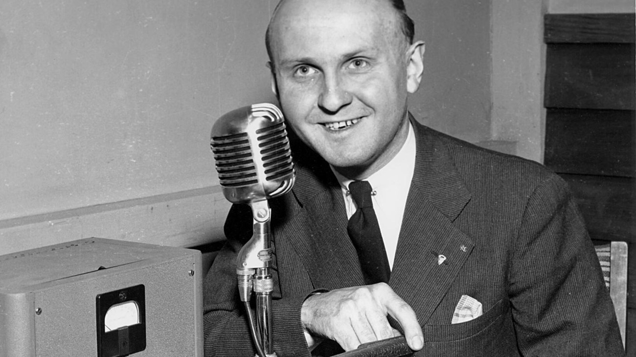 A black and white photo of a man behind a microphone touching a record