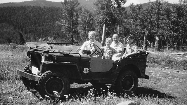 A black and white photo of a jeep with an adult and several children.
