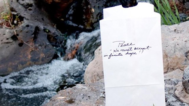 A white bag on a rock near a stream with Peace we must accept in infinite hope written on it