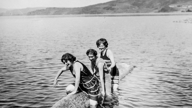 Black and white photo of 3 women in bathing suits in a large body of water.