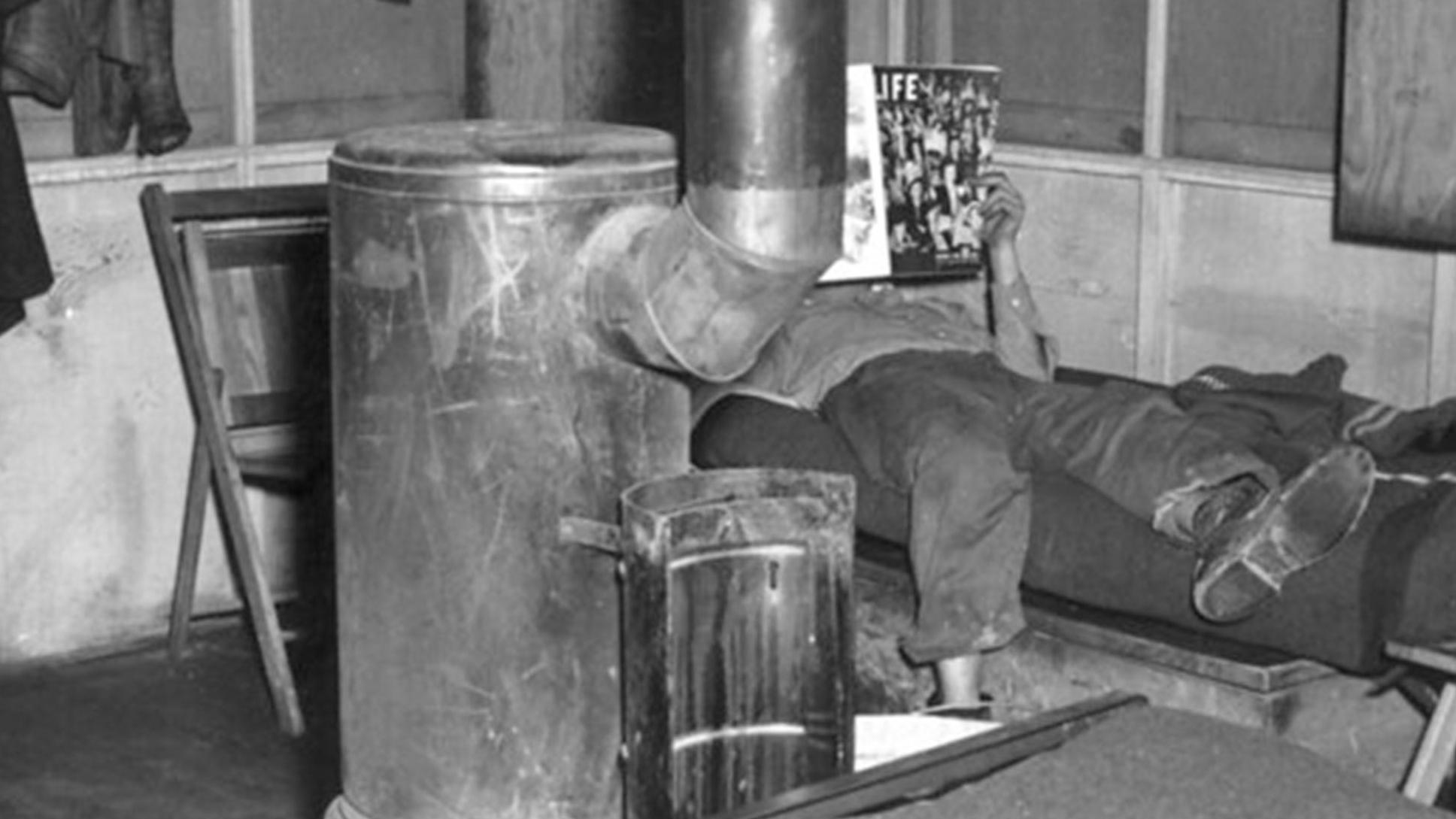 Interior of a small shack with a wood-burning stove at center. 