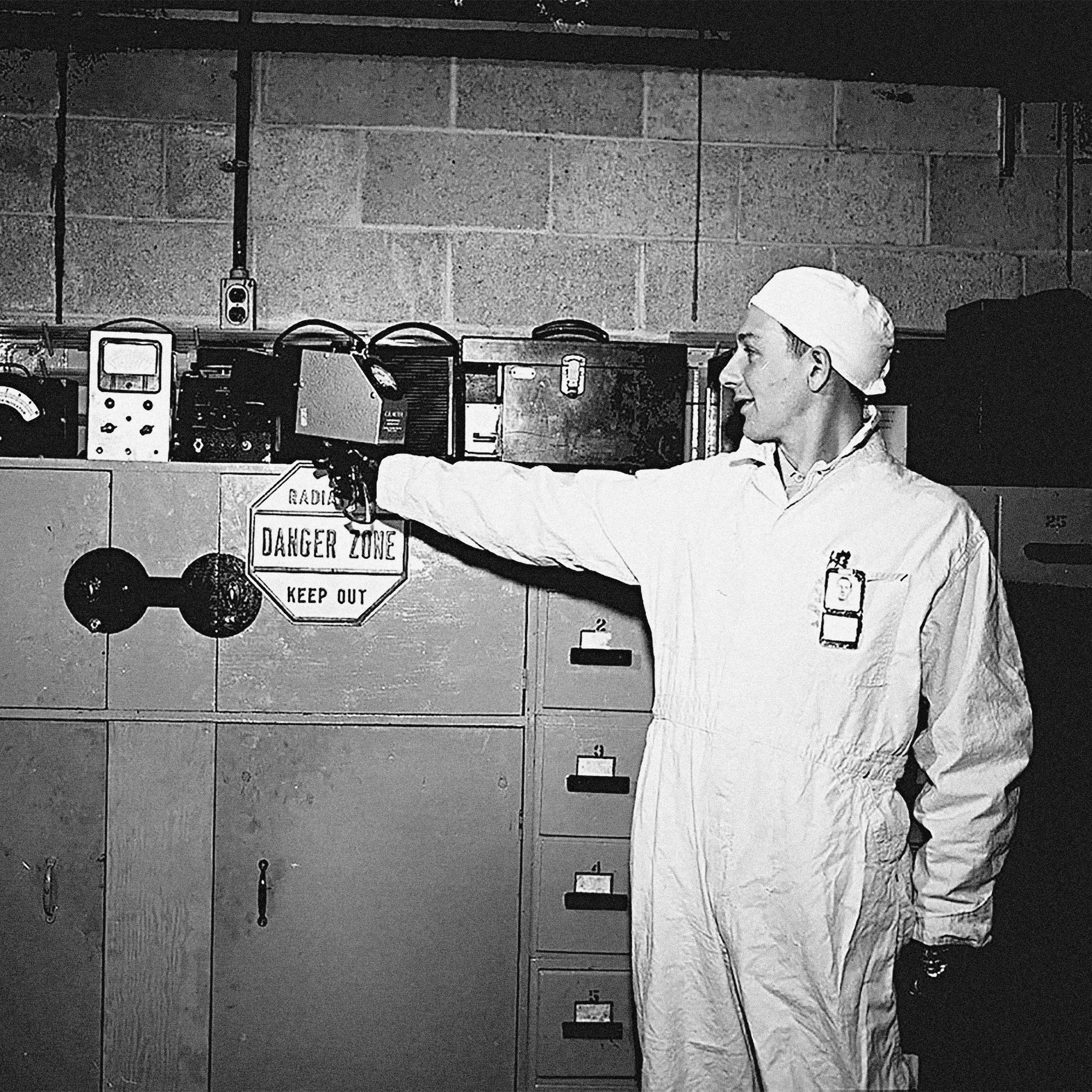 A man holds a radiation detection device towards a shelf of items.