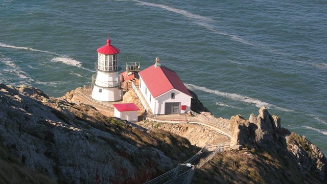 A red-roofed white lighthouse and keepers quarters surrounded by rock and water.