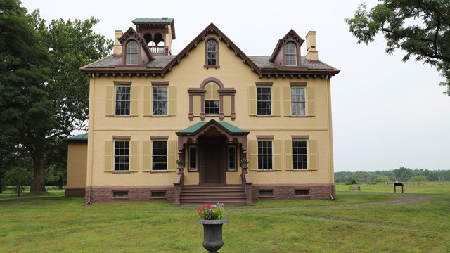 View of the historic house from the outside. Front porch, door, windows and tower are all in view.