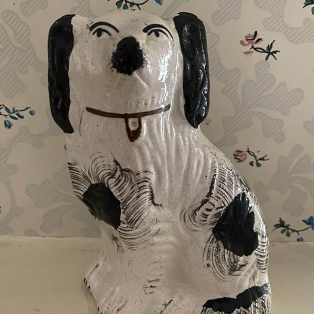 White and black ceramic Staffordshire dog figurine with painted details, in front of floral paper.
