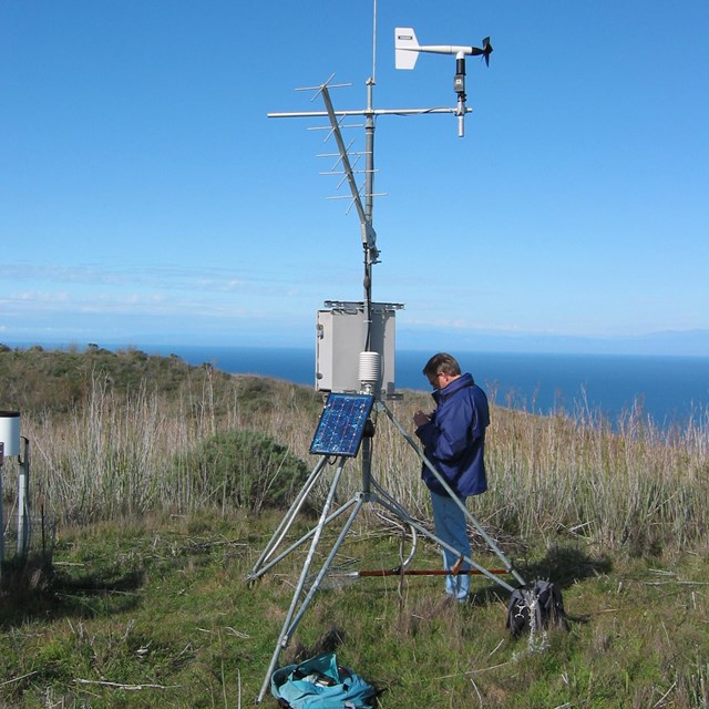 Person standing alongside a weather station atop a hill overlooking the ocean in Channel Islands NP