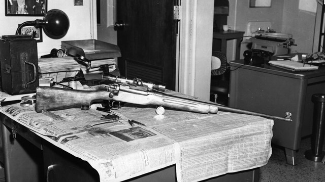 Rifle sits atop newspapers spread on metal office desk
