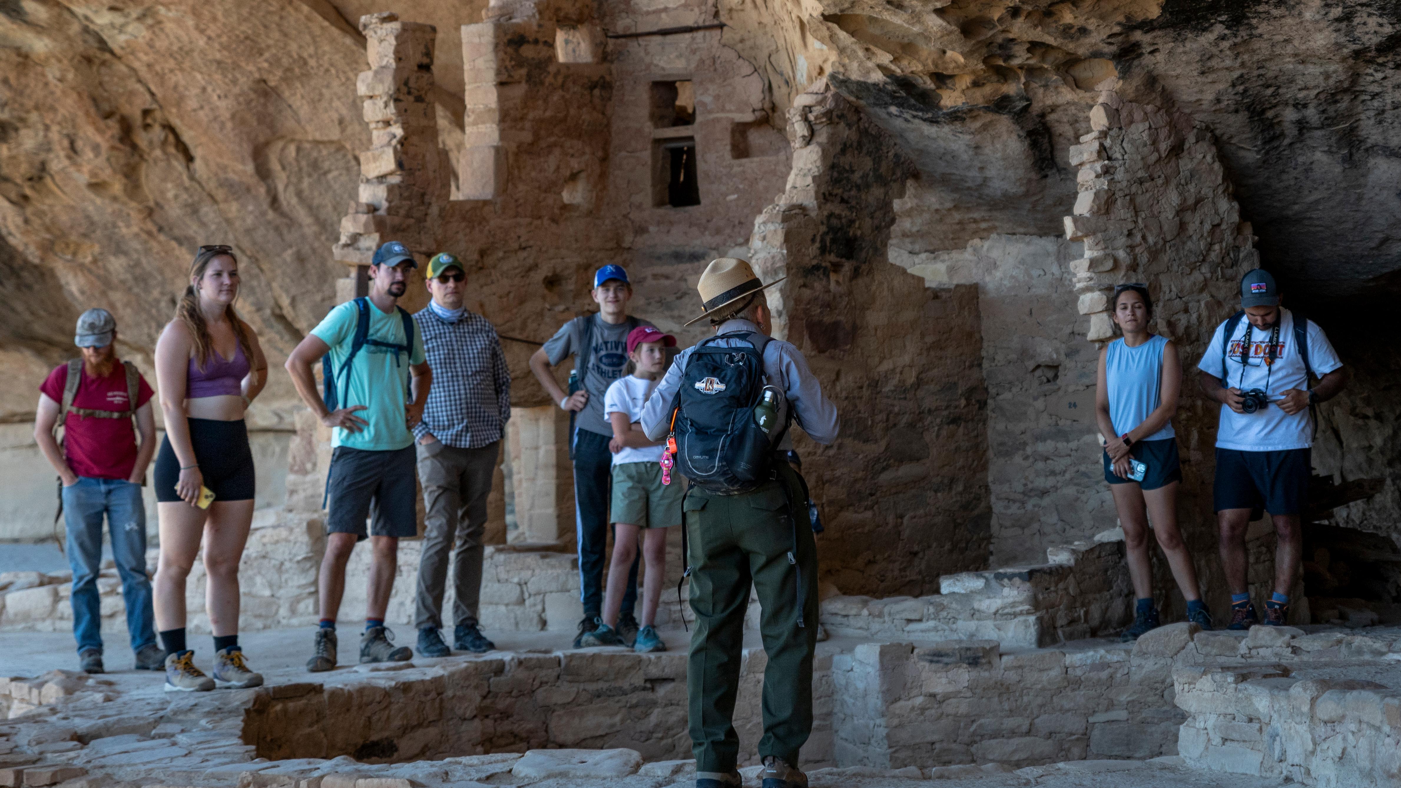 A ranger, back to the camera, stands and gestures with hands while visitors gather around listening