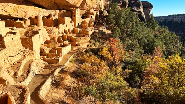 Afternoon sun glows on  an ancient sandstone village built in an alcove with leaves in autumn color