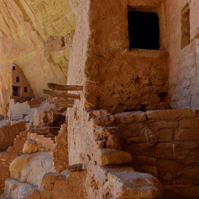 A stone masonry village and tower in a sandstone alcove with a canyon beyond
