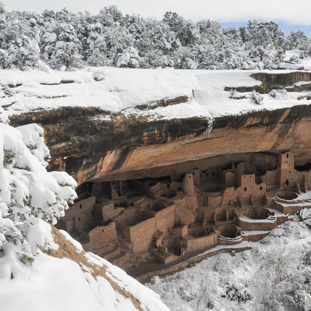 An ancestral stone-masonry village tucked into a natural cliff alcove surrounded by snowy forest